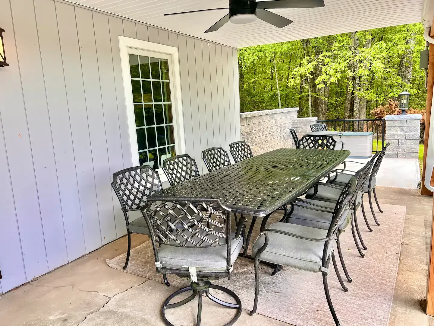 Outdoor dining set under a covered patio with a large table and multiple chairs, surrounded by trees.