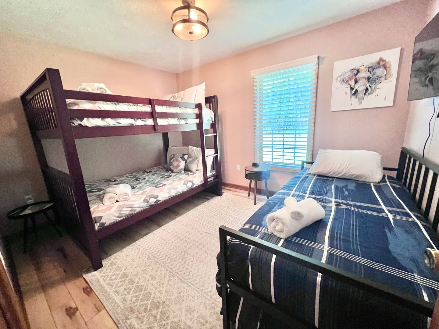 A bedroom with bunk beds and a twin bed, pink walls, and a window with blinds.