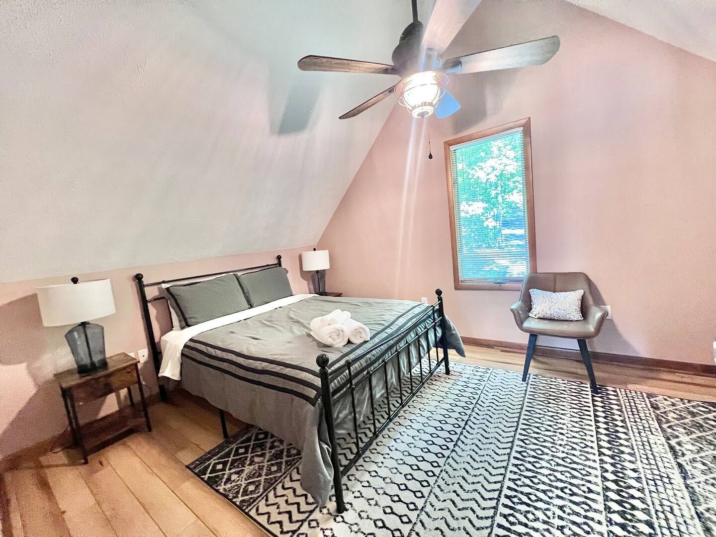 Bedroom with metal bed frame, rug, chair, and a window. Pink walls and wood floor.