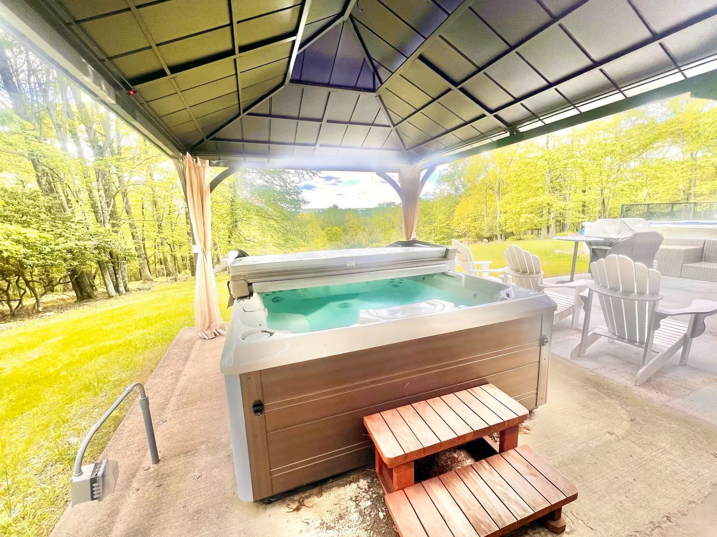 Hot tub under a gazebo with a view of trees. Wooden steps lead up to the tub.