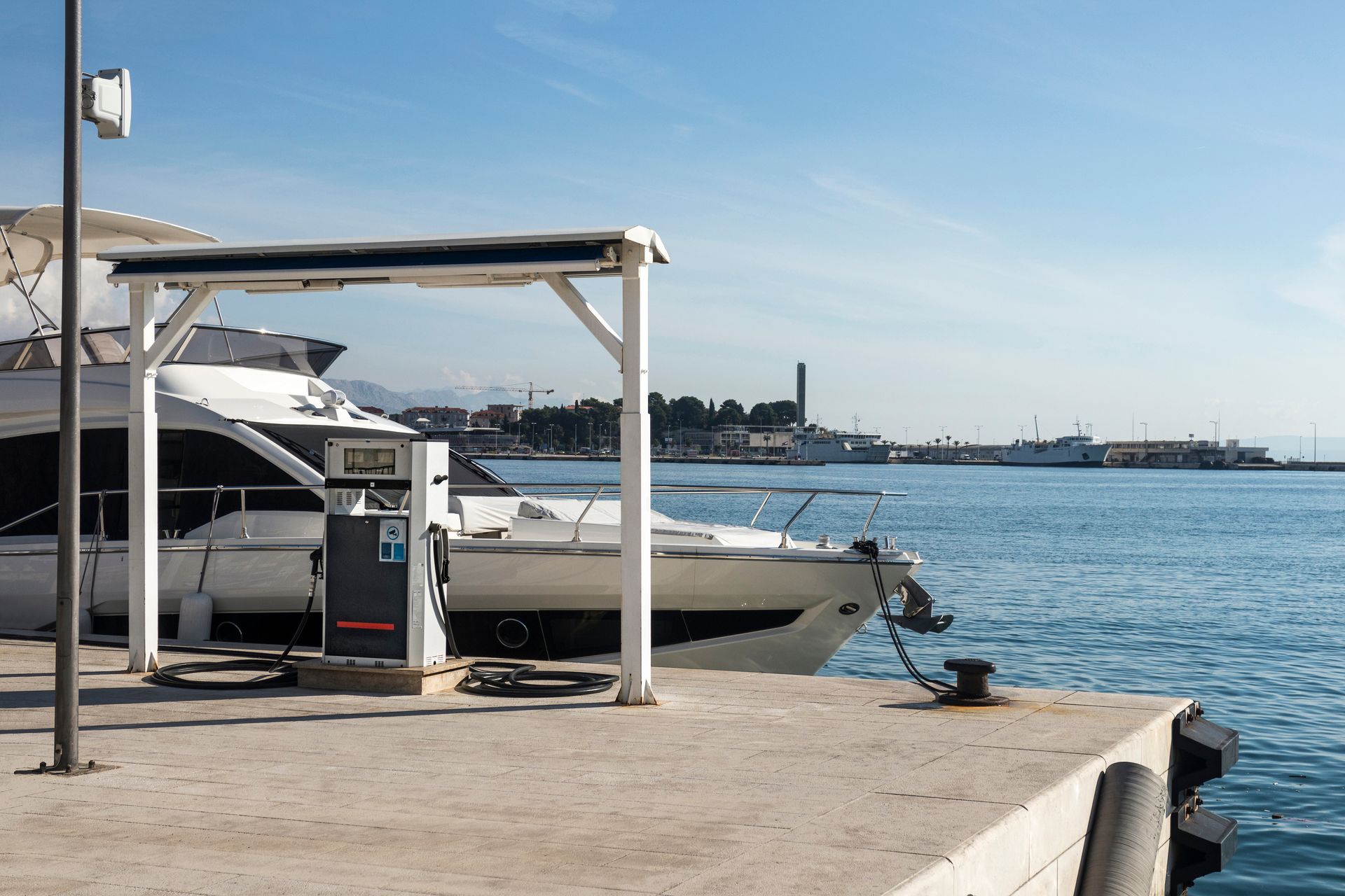 White boat docked at a sunny marina with open water and distant shoreline under a clear sky