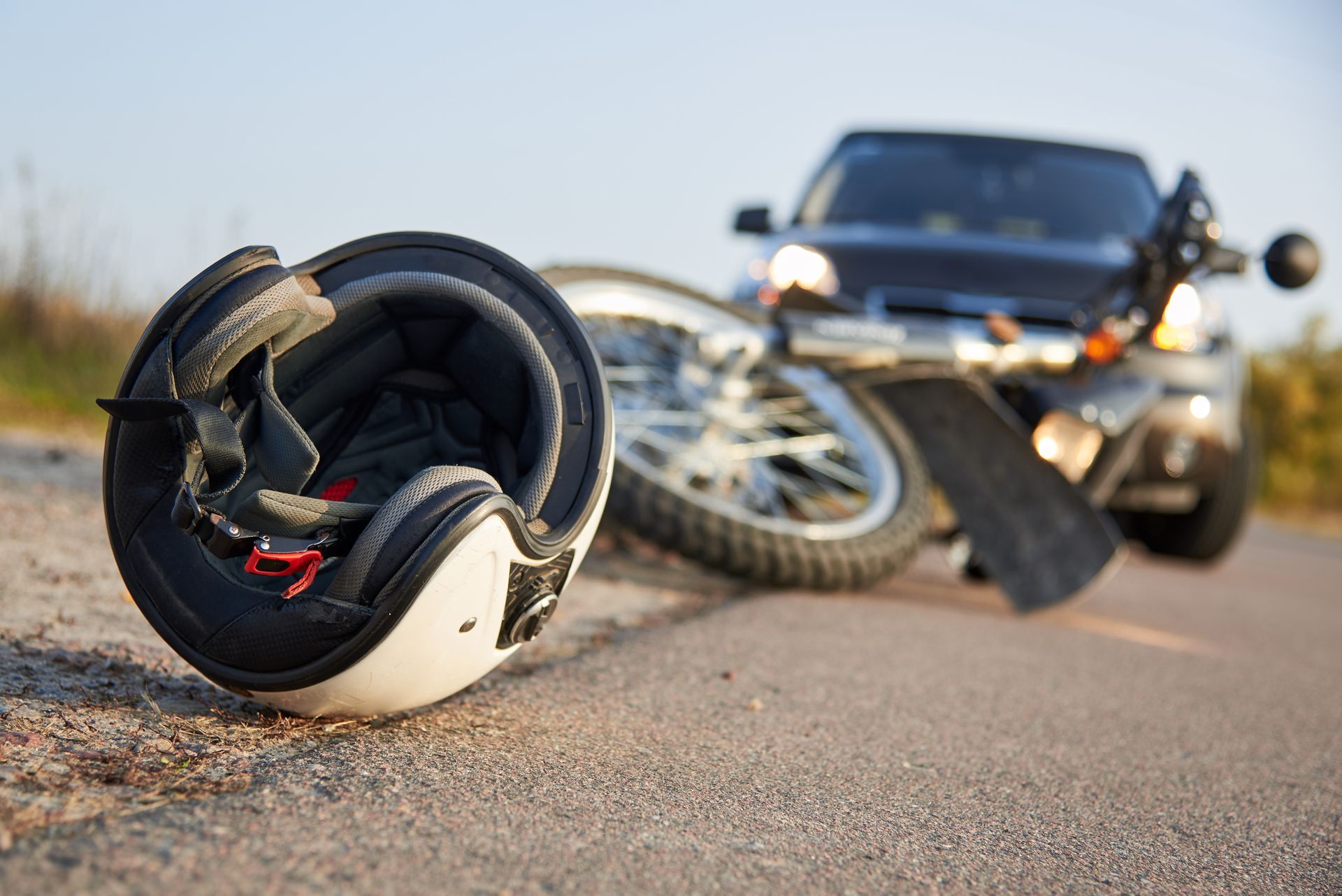 Overturned motorcycle helmet on road, with a crashed motorcycle and car in the background.