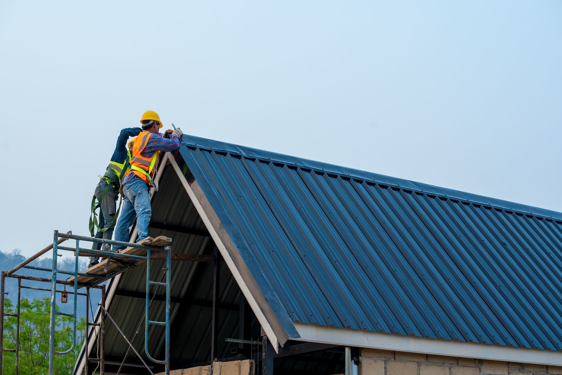 Worker on scaffolding installing blue metal roofing on a house roof