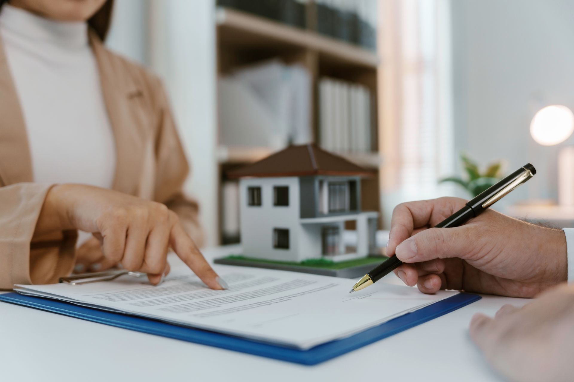 Hands and pen reviewing a contract beside a model house on a desk