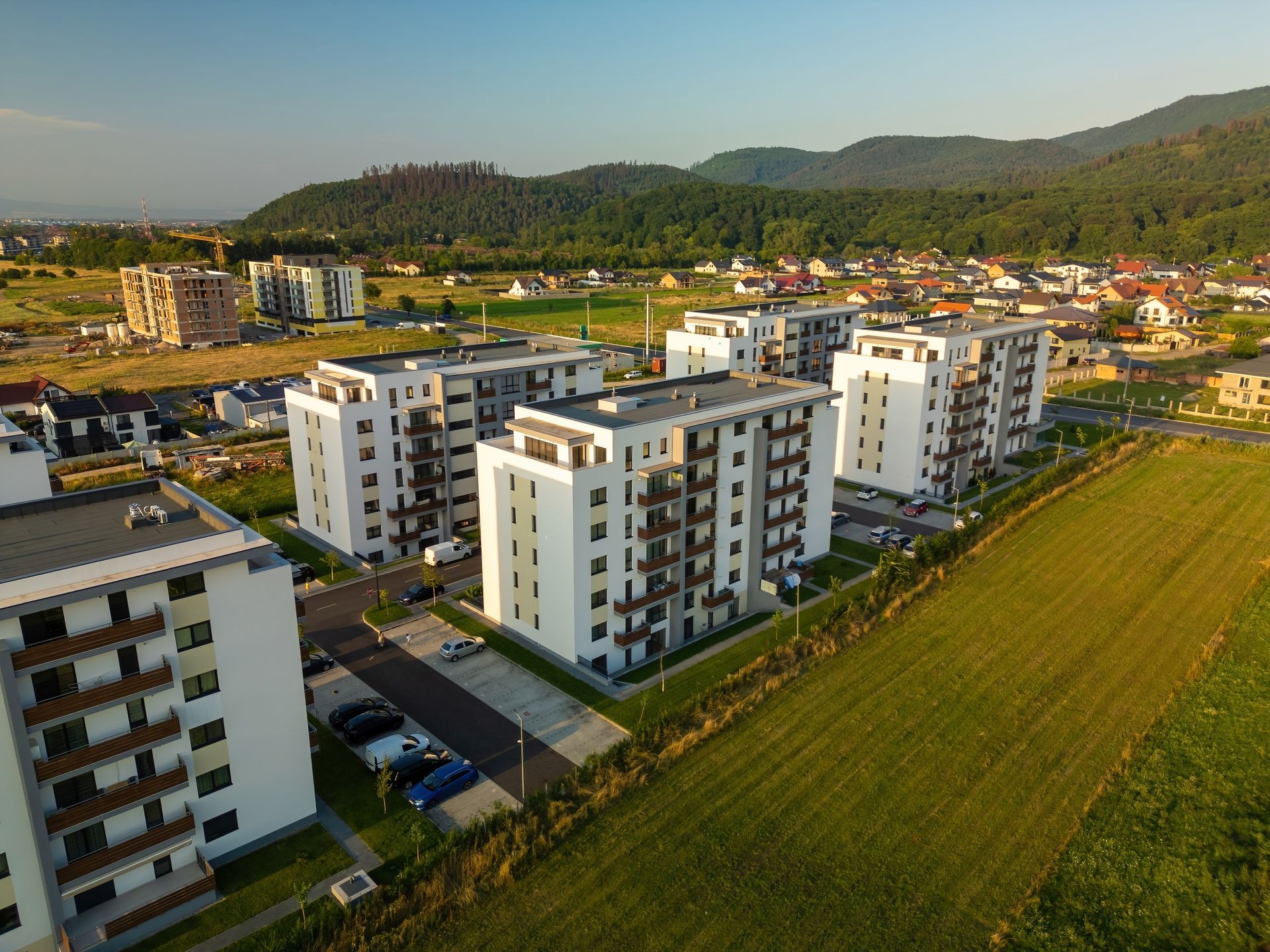 Aerial view of white apartment buildings beside green fields and hills at sunset
