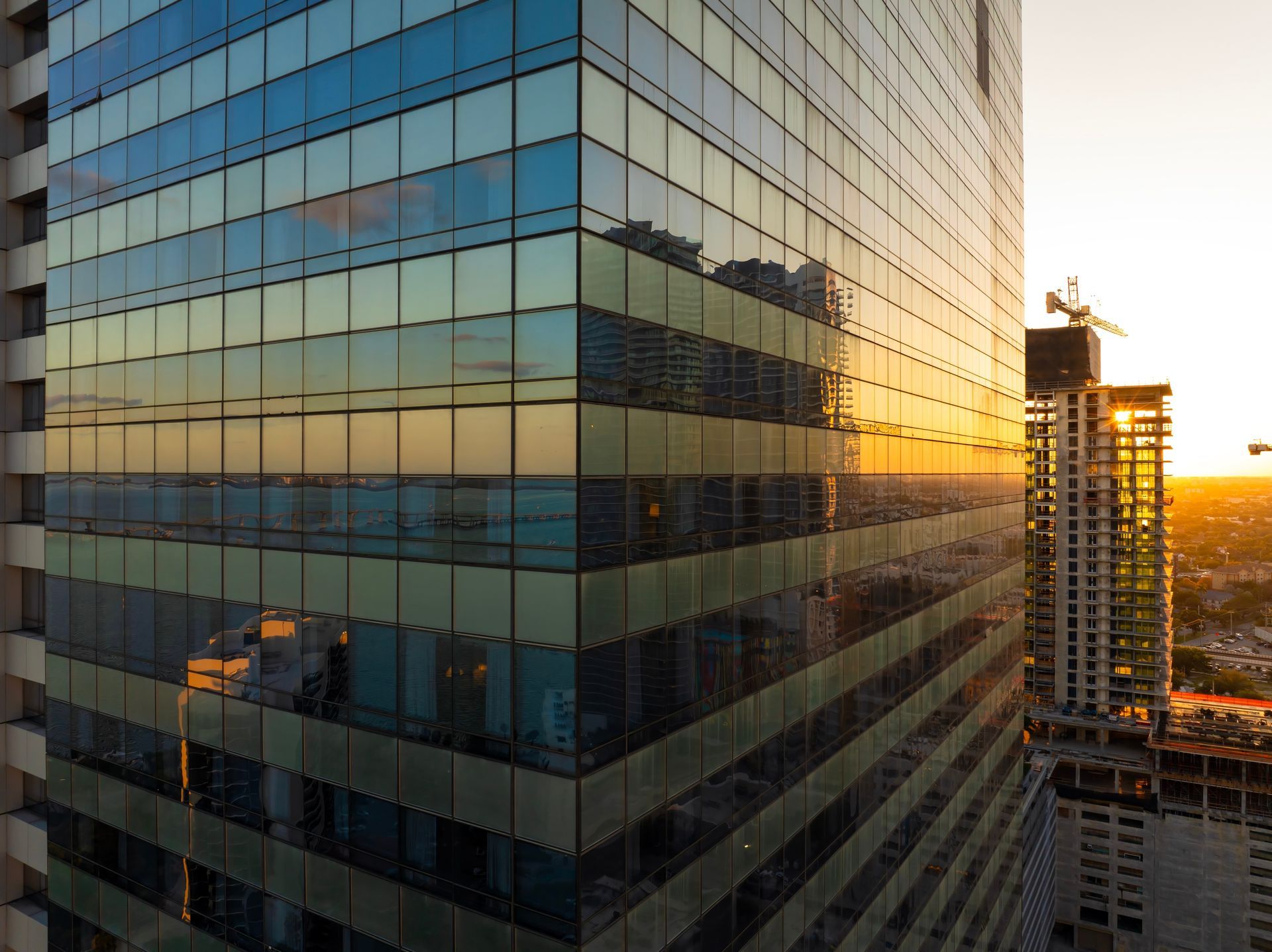 Glass office building at sunset reflecting warm golden light in an urban skyline