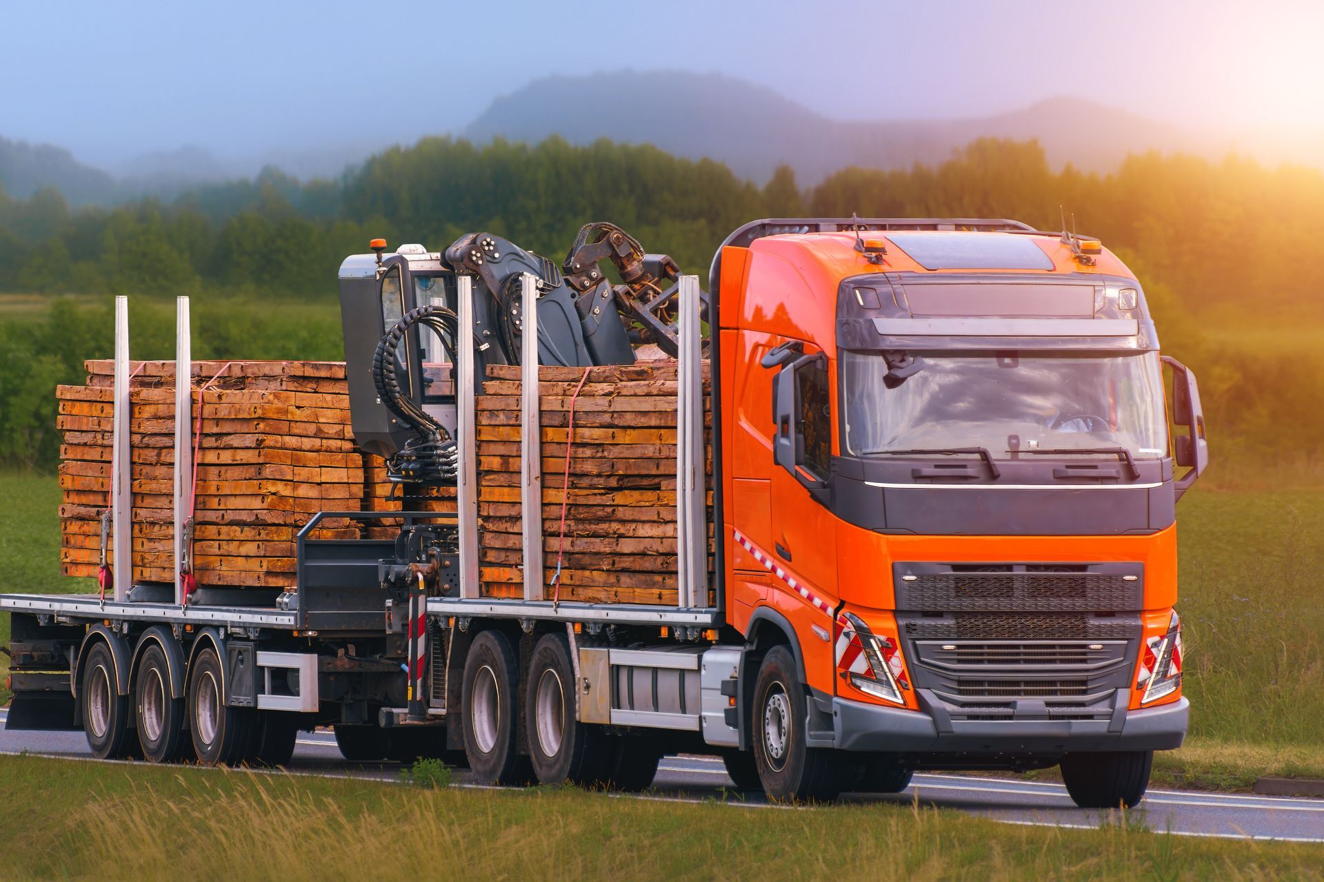 Orange logging truck hauling stacked timber on a road at sunset