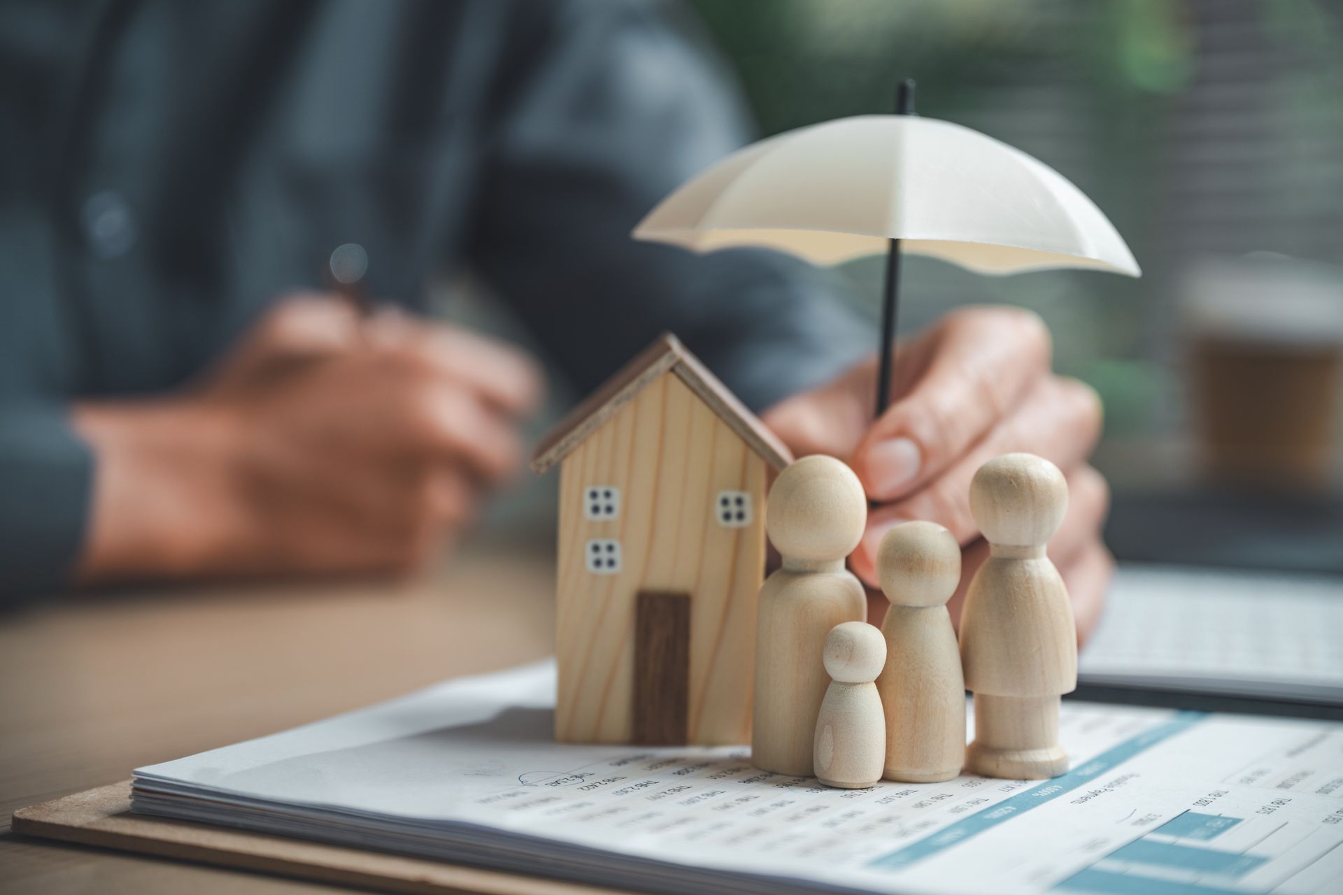Miniature house and family figures under a white umbrella, symbolizing home insurance protection