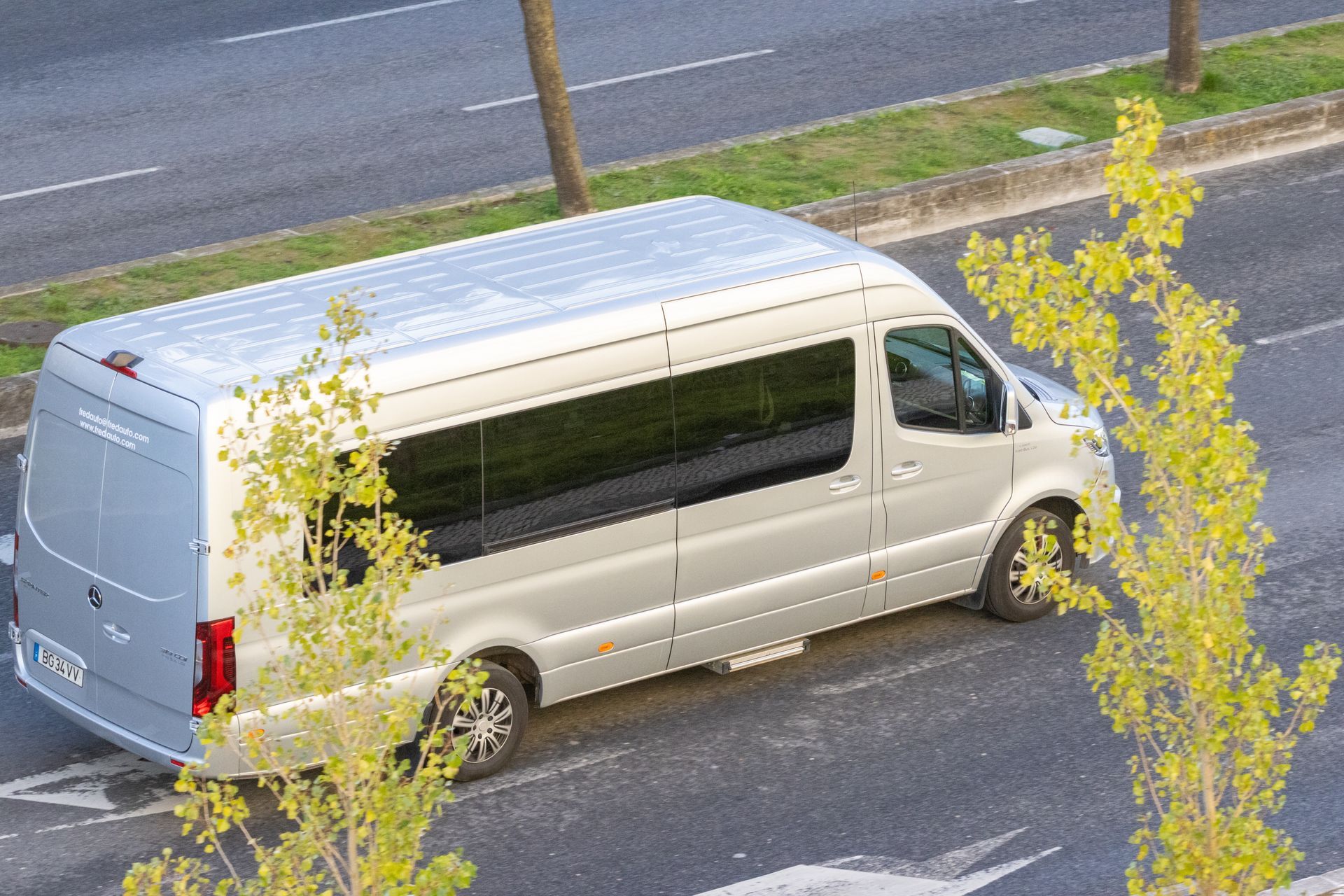 White van parked on a wet roadside beside a road, partly obscured by yellow-leaved trees.