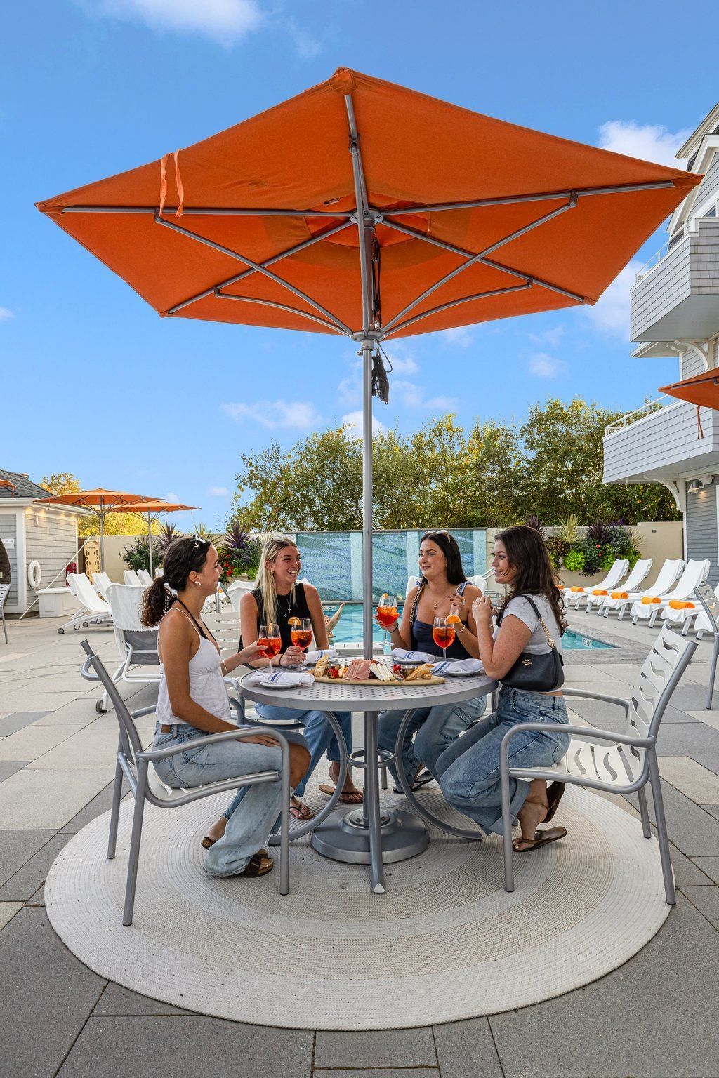 A group of women are sitting at a table under an orange umbrella.