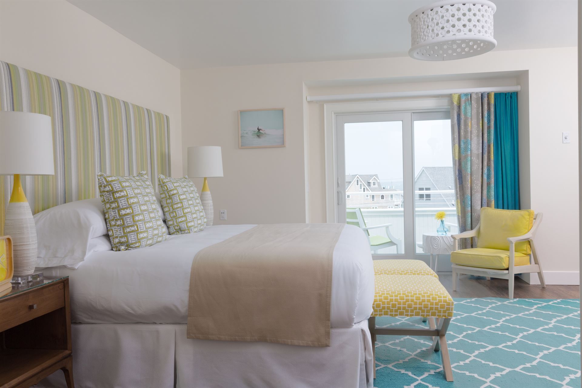 A hotel room with a king size bed , chairs , lamps and a sliding glass door.