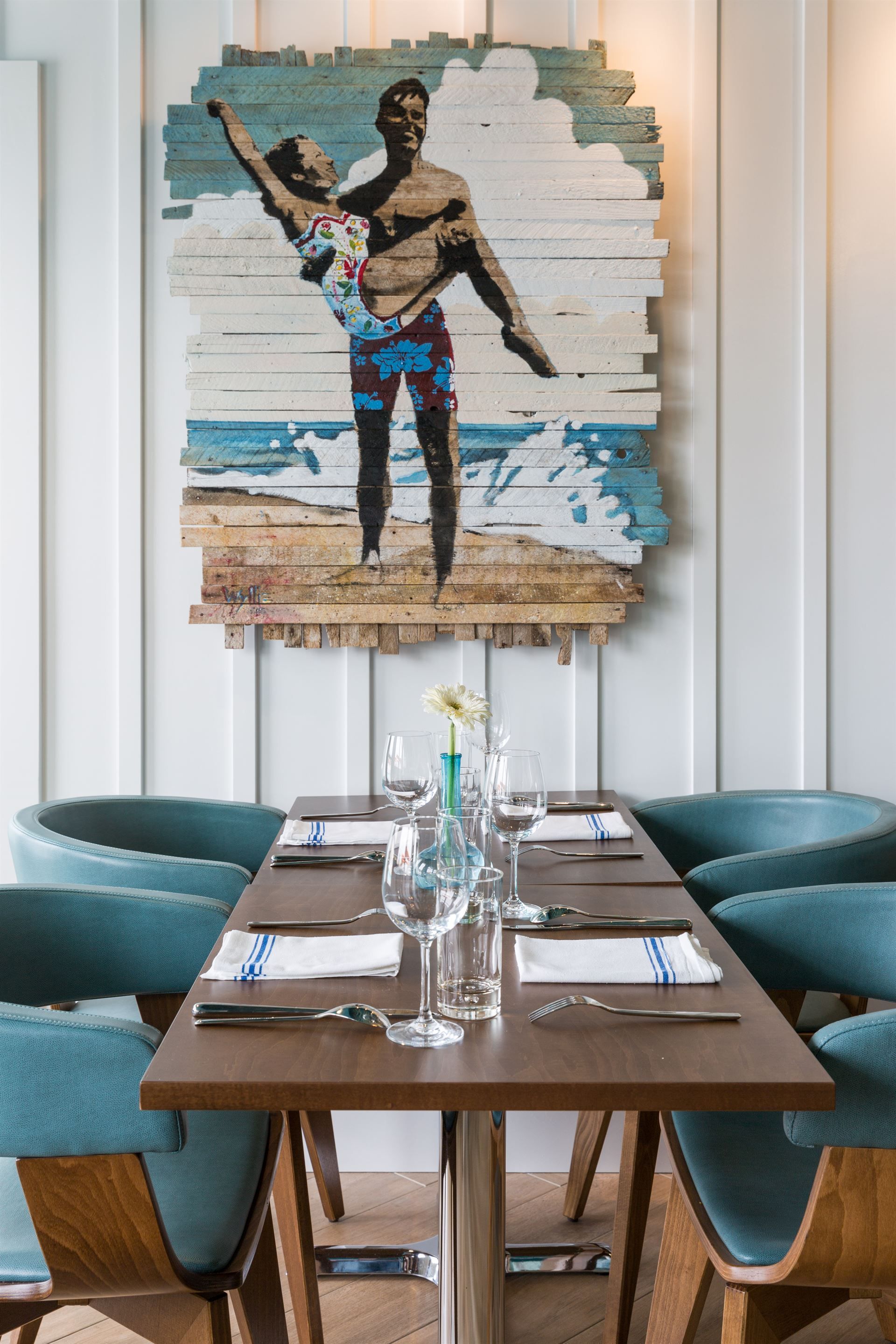 A dining room with a table and chairs and a painting on the wall.