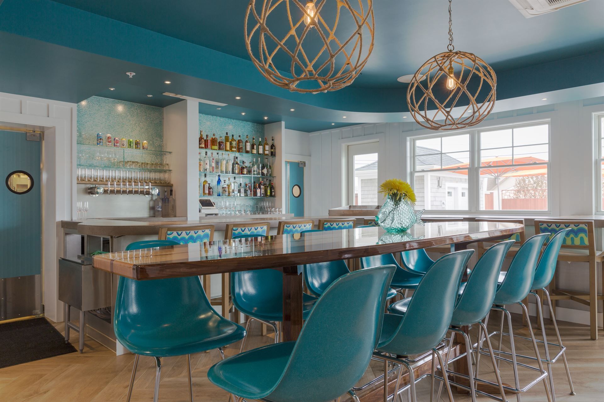 A restaurant with a long table and blue chairs and a bar.