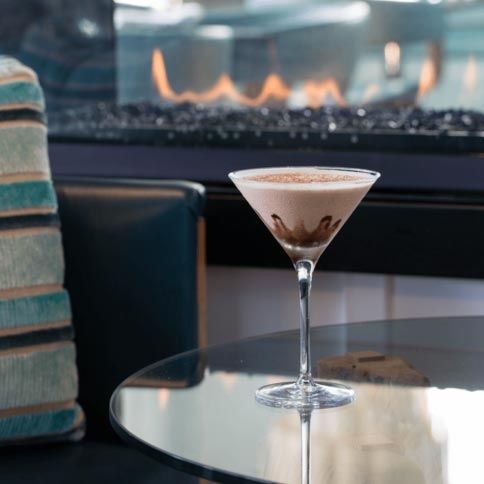 A martini is on a table in front of a fireplace