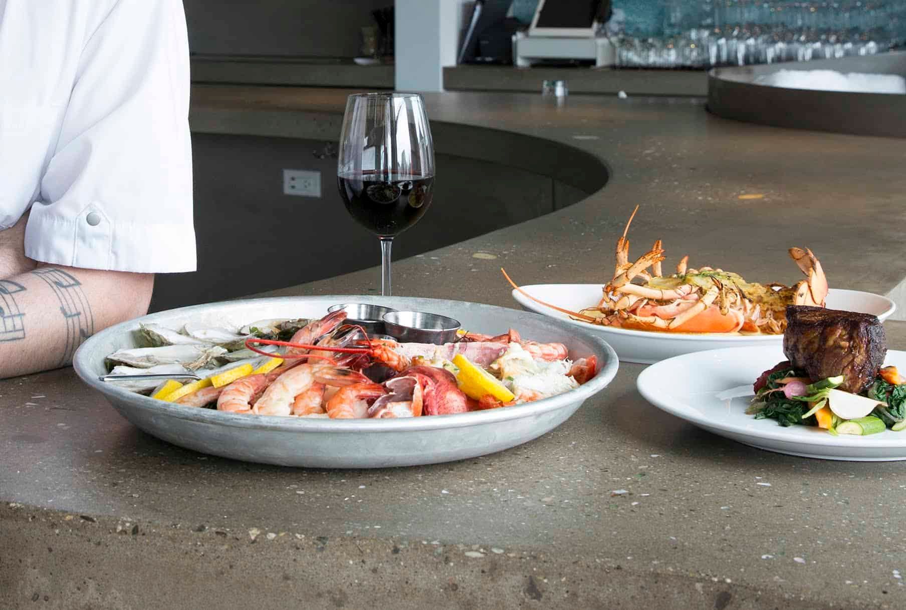 A person is sitting at a table with plates of food and a glass of wine.