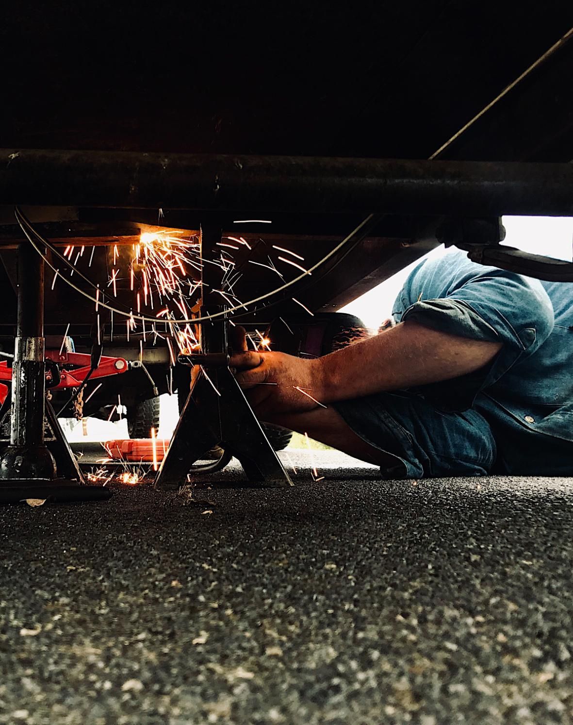 A man is working under a car with a welding machine.
