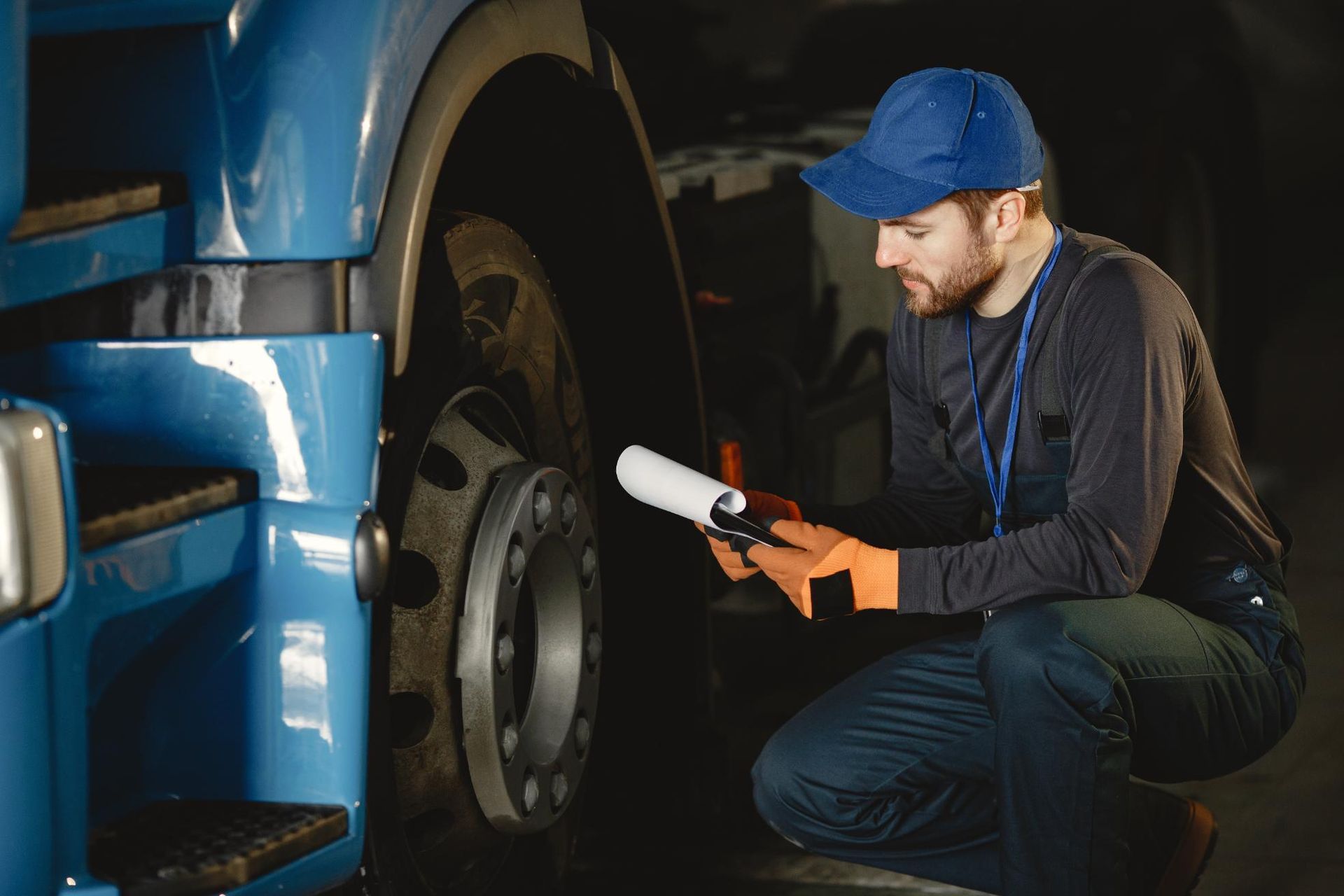 A man is kneeling down next to a blue truck and looking at a clipboard.