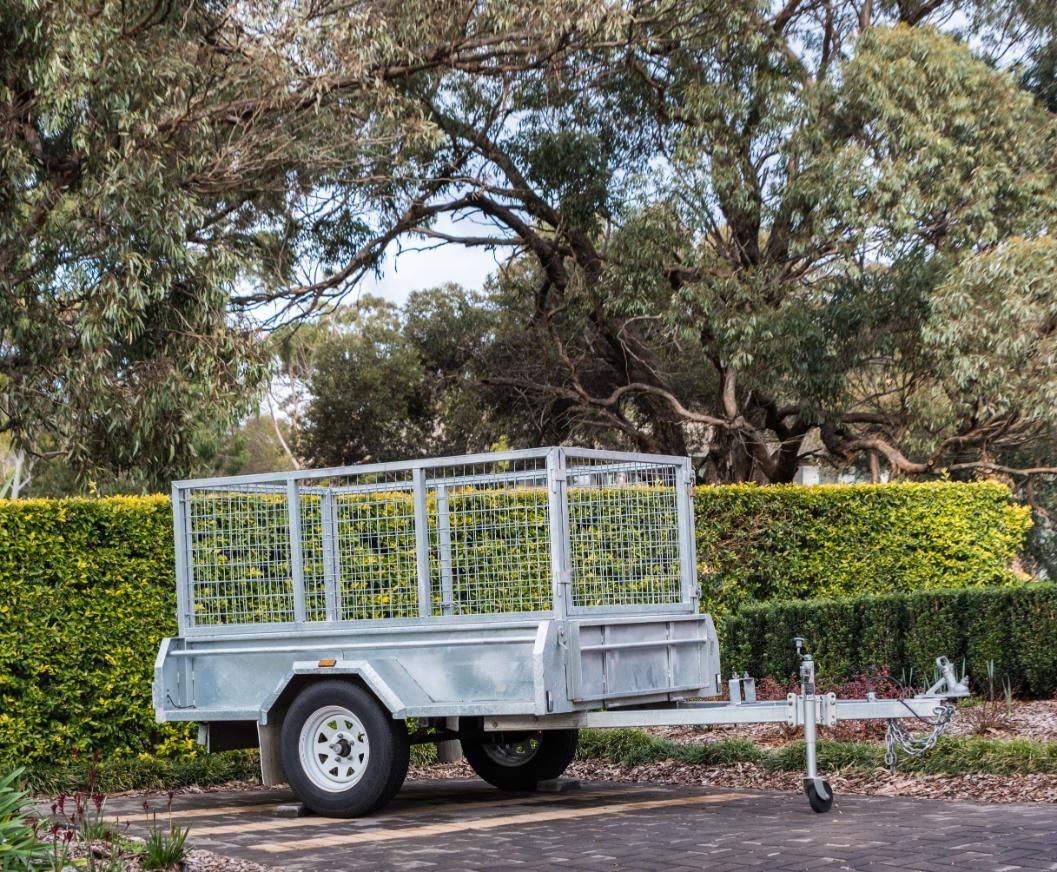 A trailer is parked on the side of the road in front of a hedge.