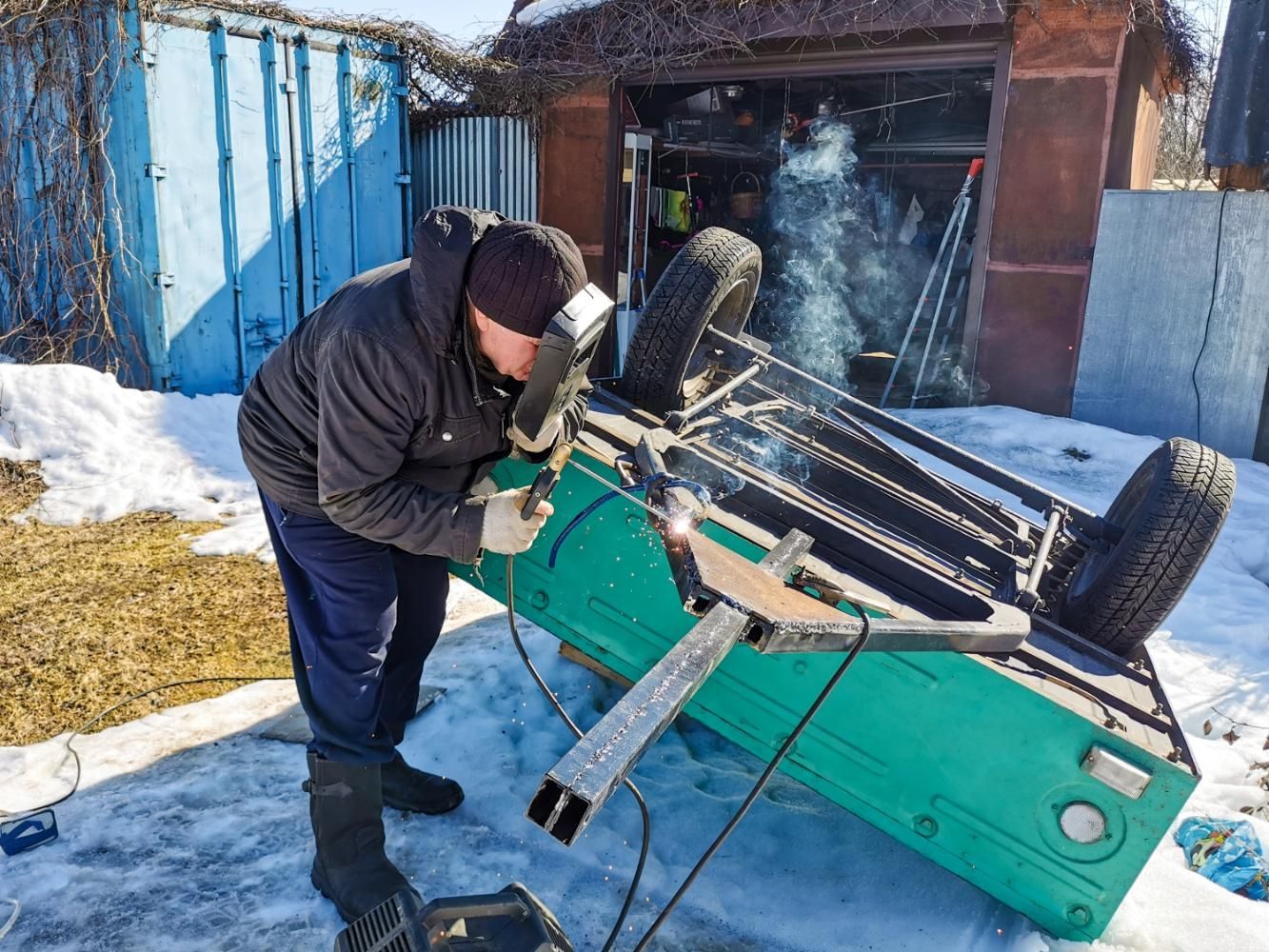 A man is welding a green vehicle in the snow.