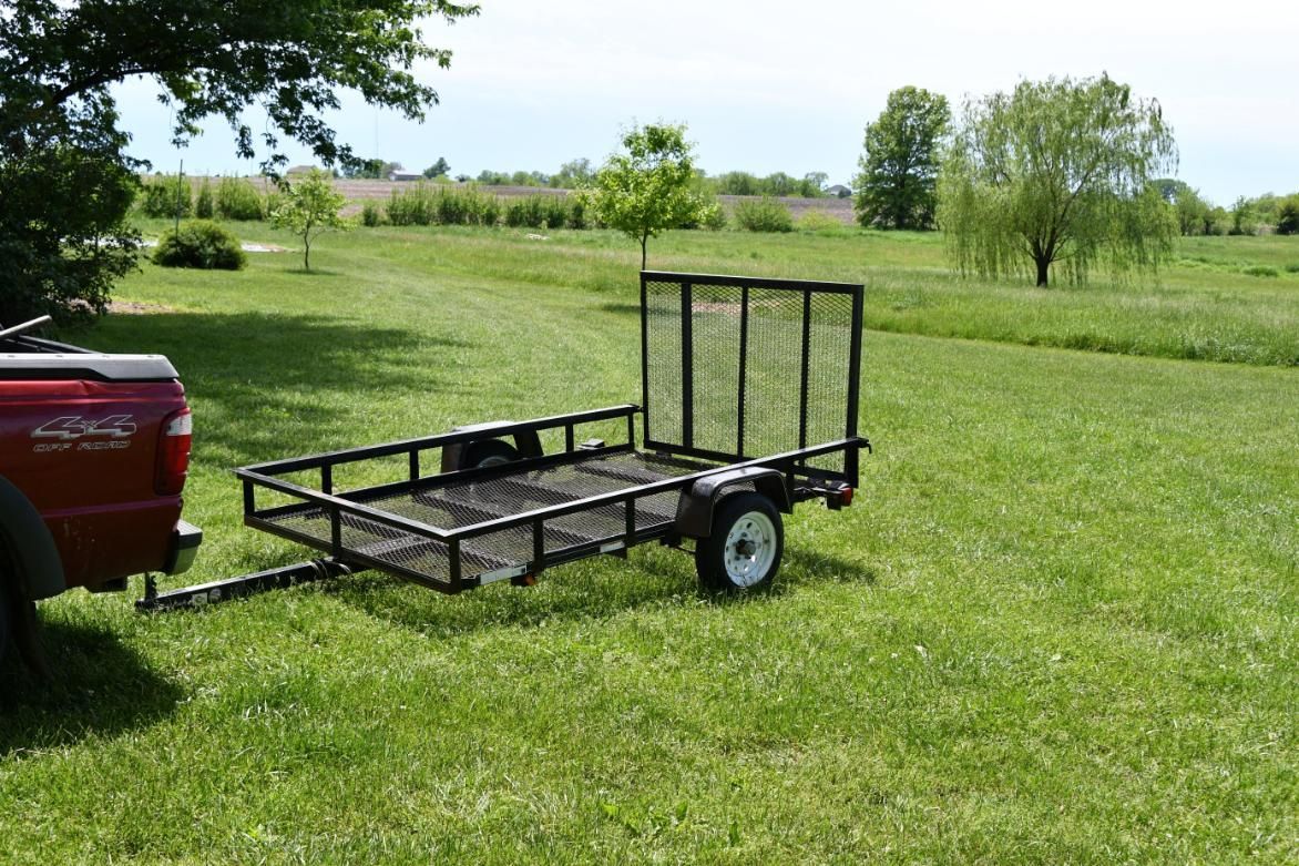 A red truck is towing a small trailer in a grassy field.