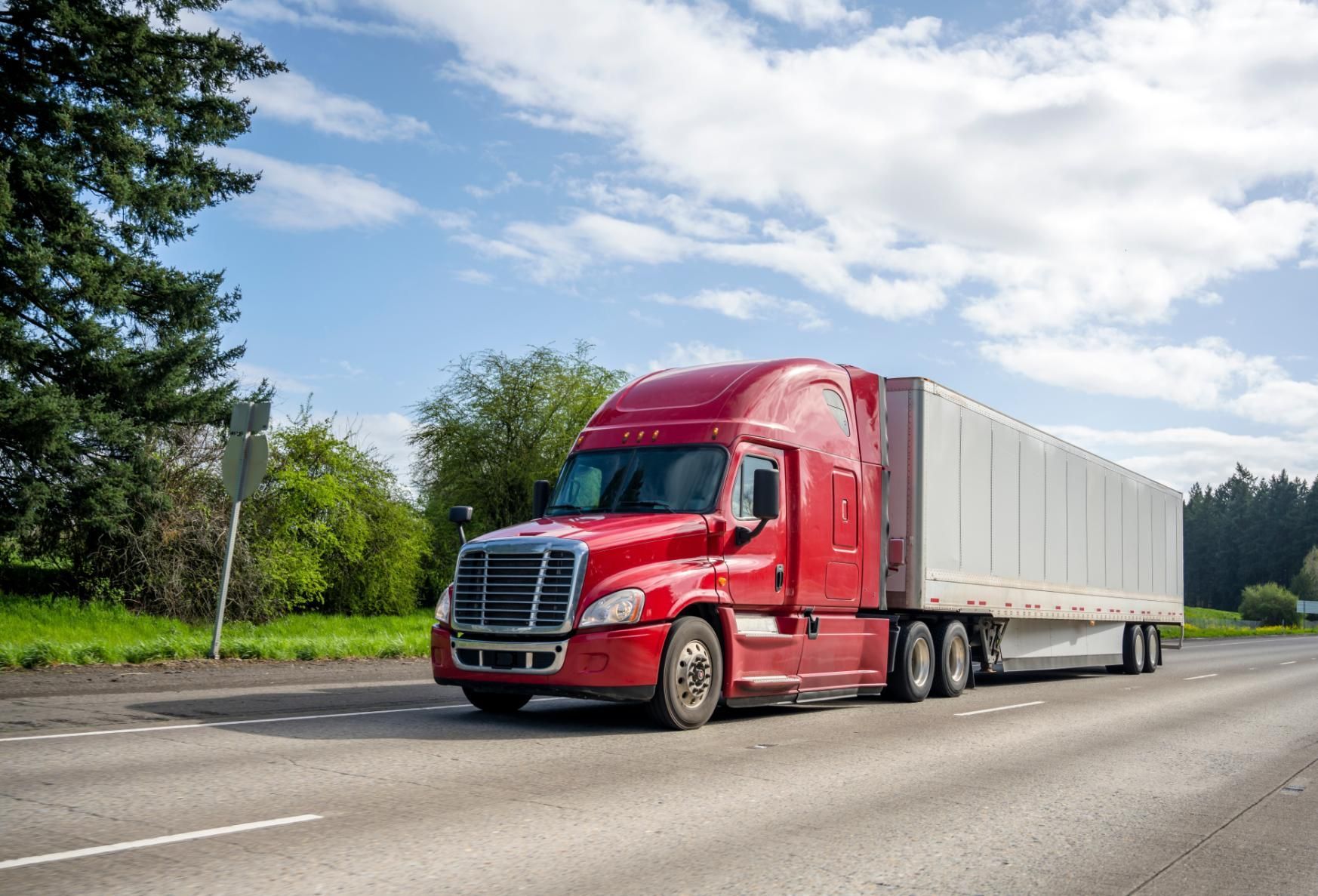 A red semi truck is driving down a highway.