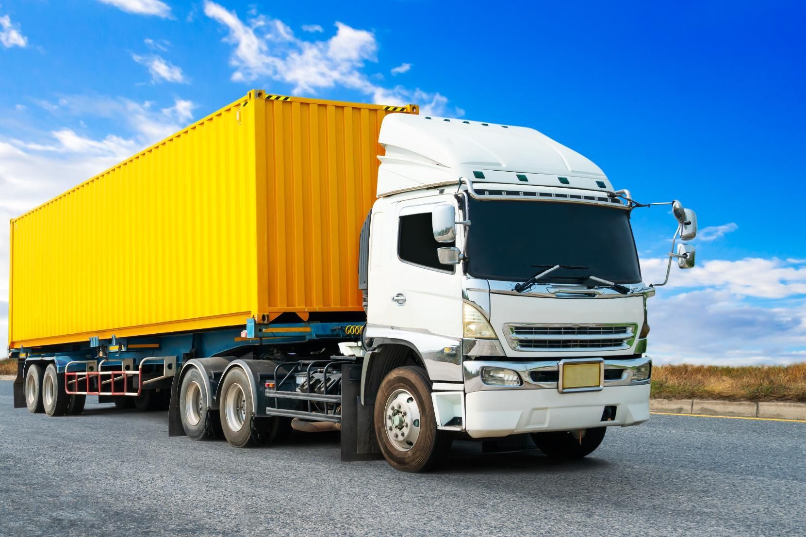 A white semi truck with a yellow trailer is driving down a road.