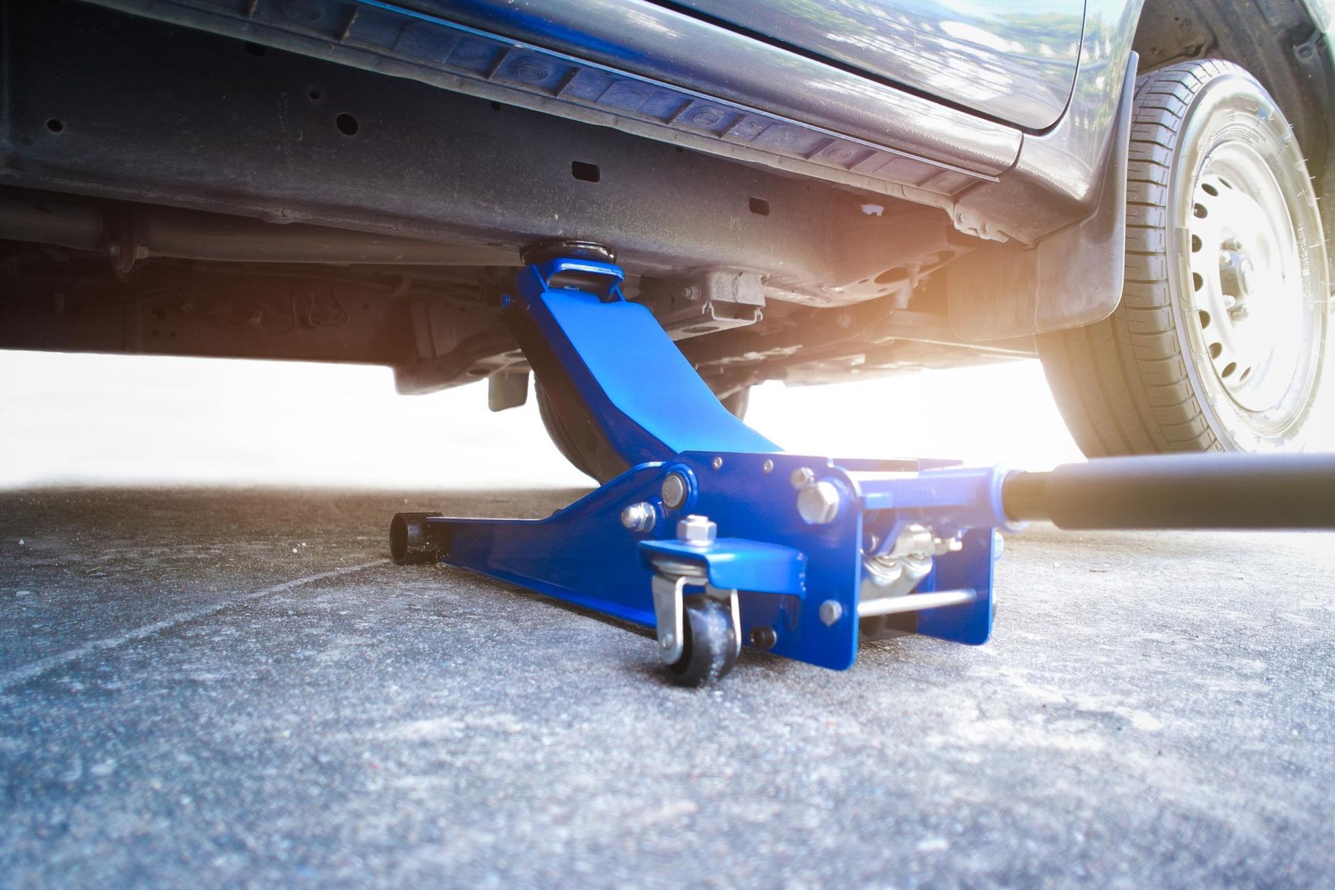 A blue floor jack is sitting under a car on the ground.