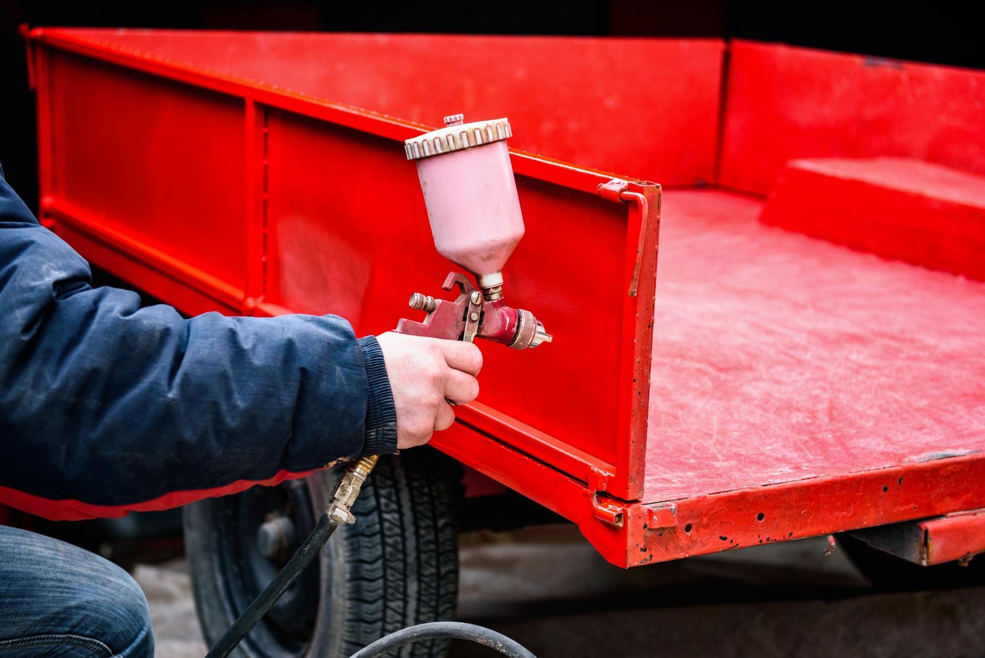 A man is spraying paint on a red trailer.