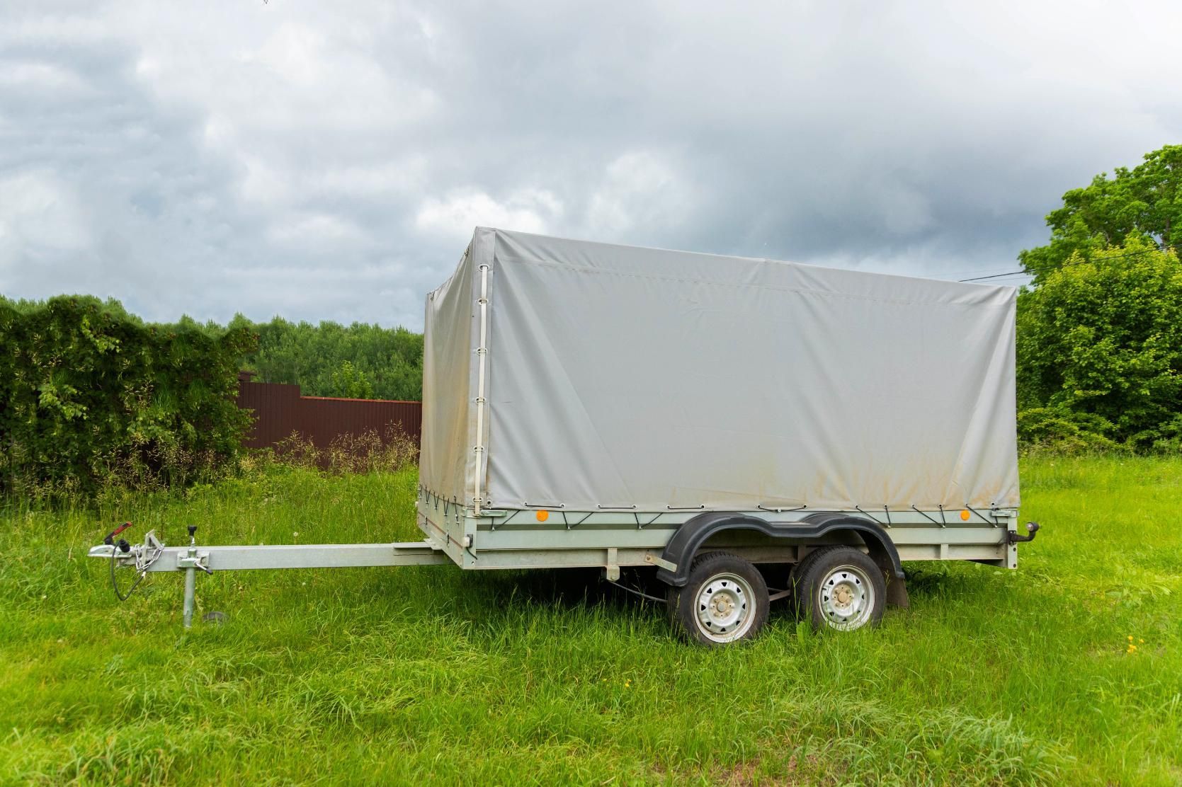 A trailer with a tarp on it is parked in a grassy field.