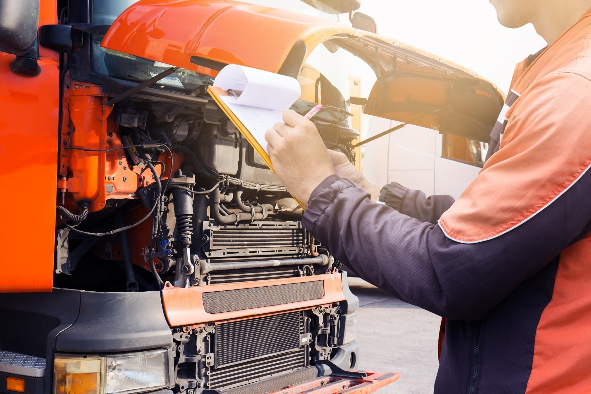 A man is writing on a clipboard in front of an orange truck.