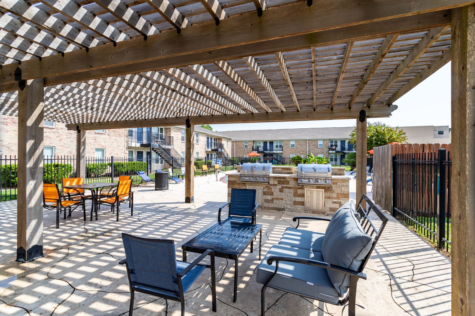 A patio area with tables and chairs under a pergola at Baystone Apartments in Webster, TX.