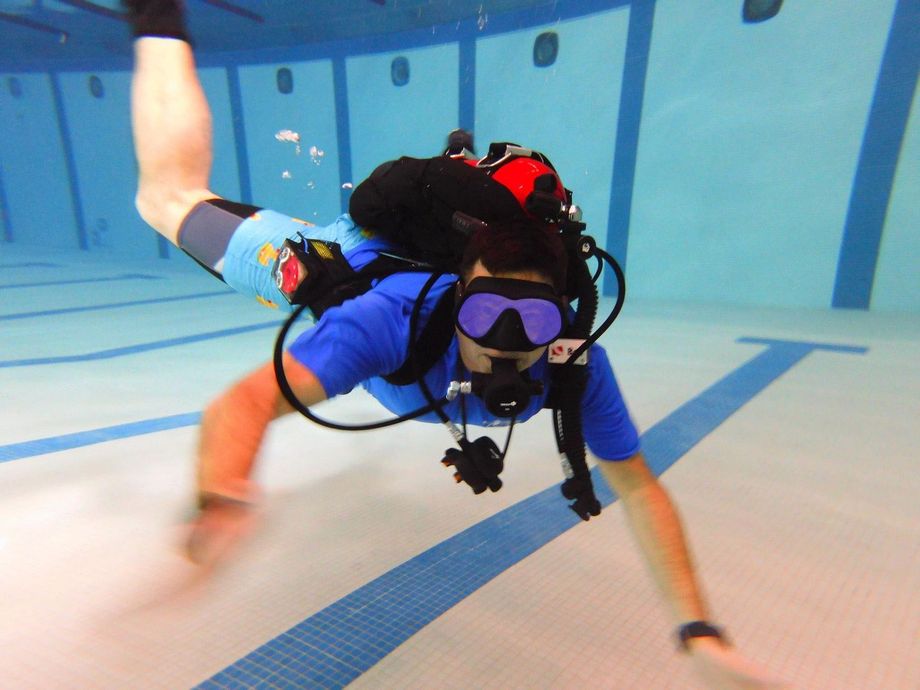 A scuba diver is doing a handstand in a pool