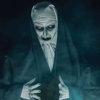 A nun with a scary face painted on her face is holding a rosary.