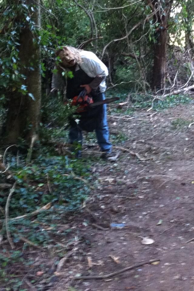 Man wearing an apron and wielding a chainsaw in a wooded area.