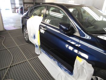 A blue car is being painted in a garage