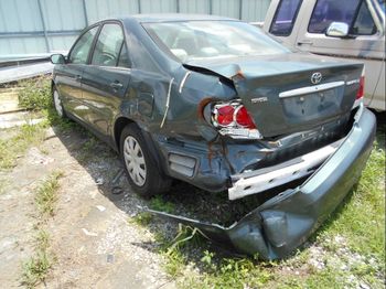 A damaged toyota camry is parked in a grassy field.