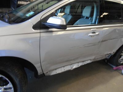 A silver car with a damaged side is parked in a garage