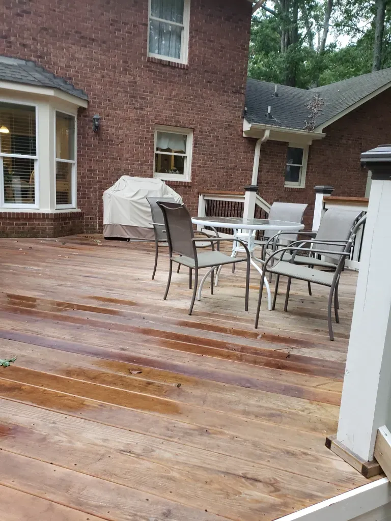 A wooden deck with a table and chairs in front of a brick house.