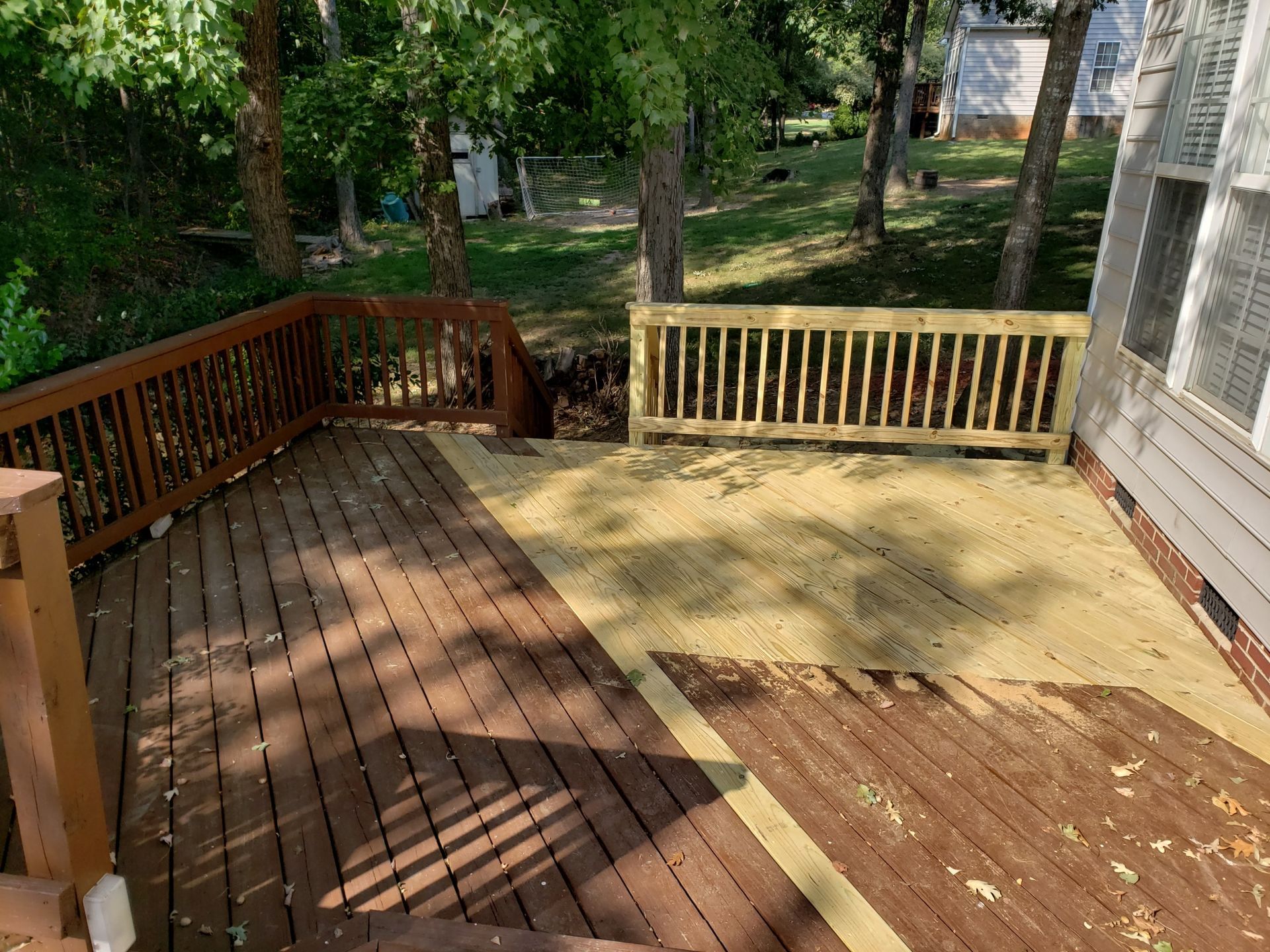 A wooden deck with a wooden railing in the backyard of a house.