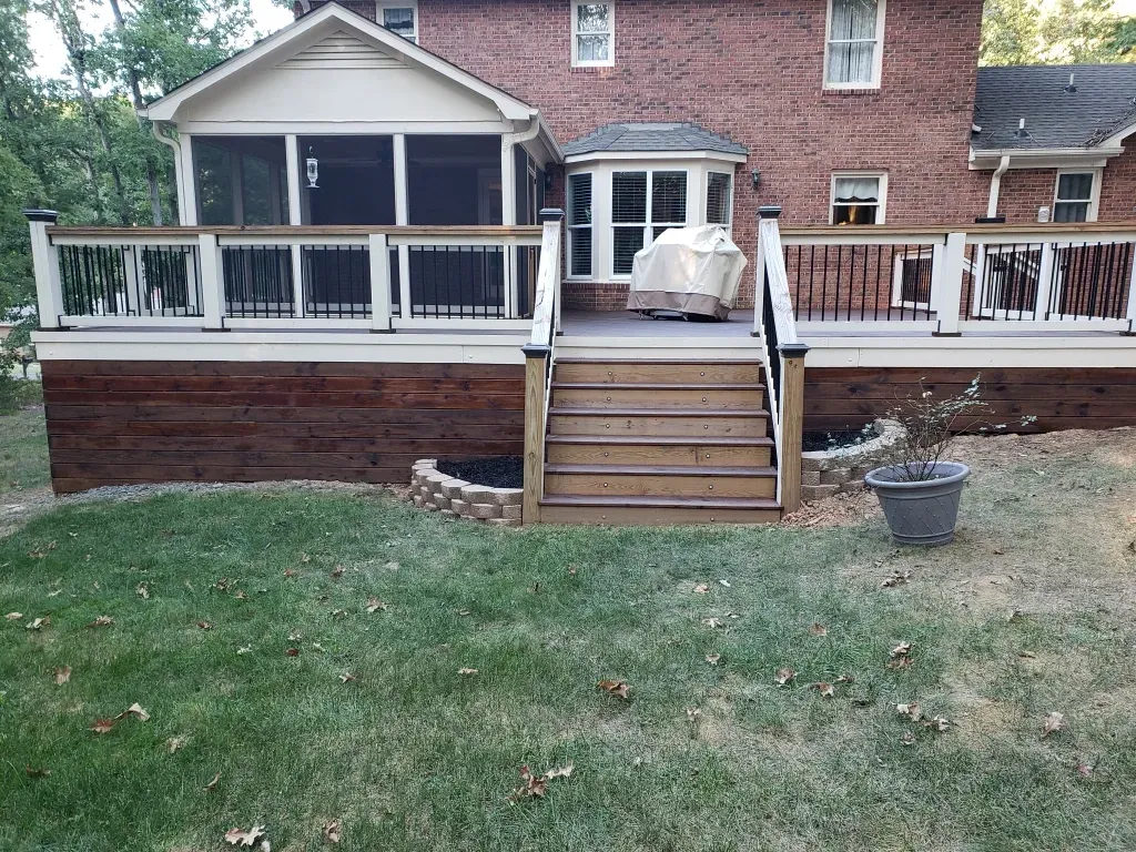 A brick house with a screened in porch and a wooden deck.