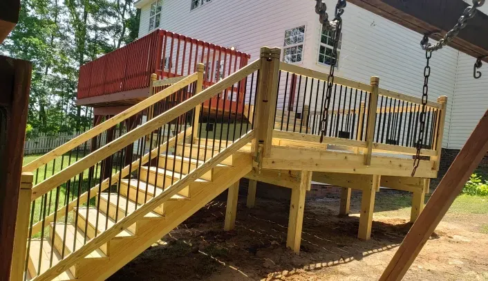 A wooden deck with stairs and a swing set in front of a house.