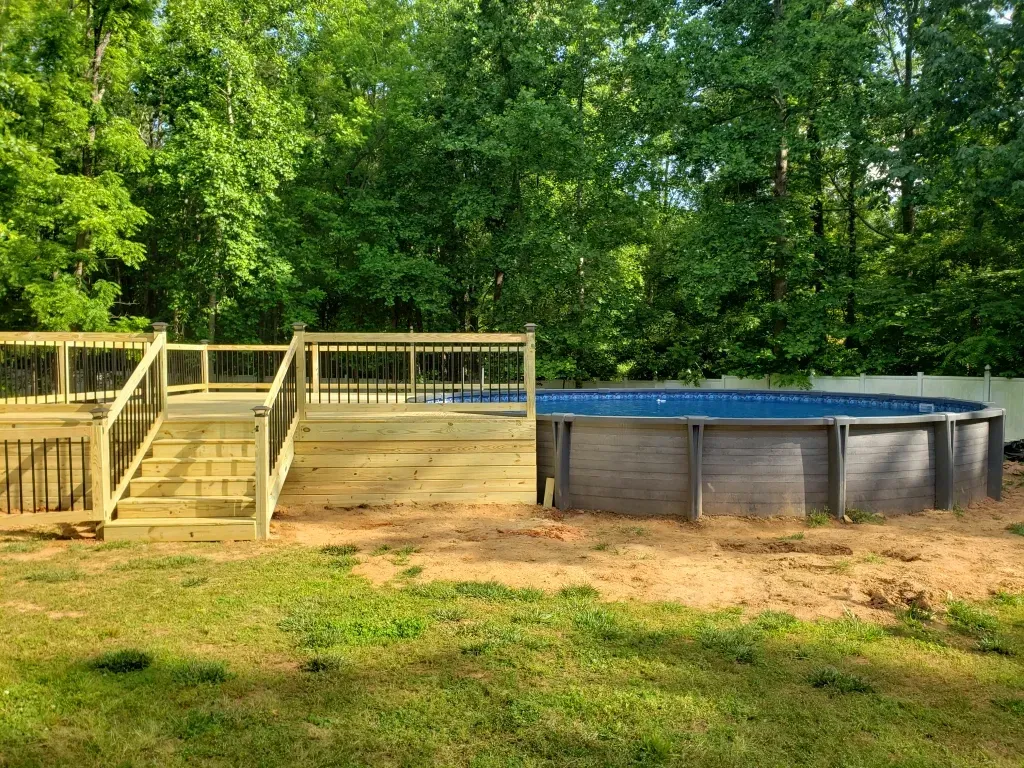 A large swimming pool with a wooden deck and stairs surrounded by trees.