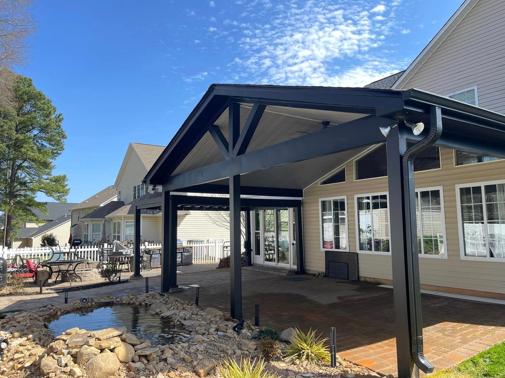 A large house with a covered porch and a pond in front of it.