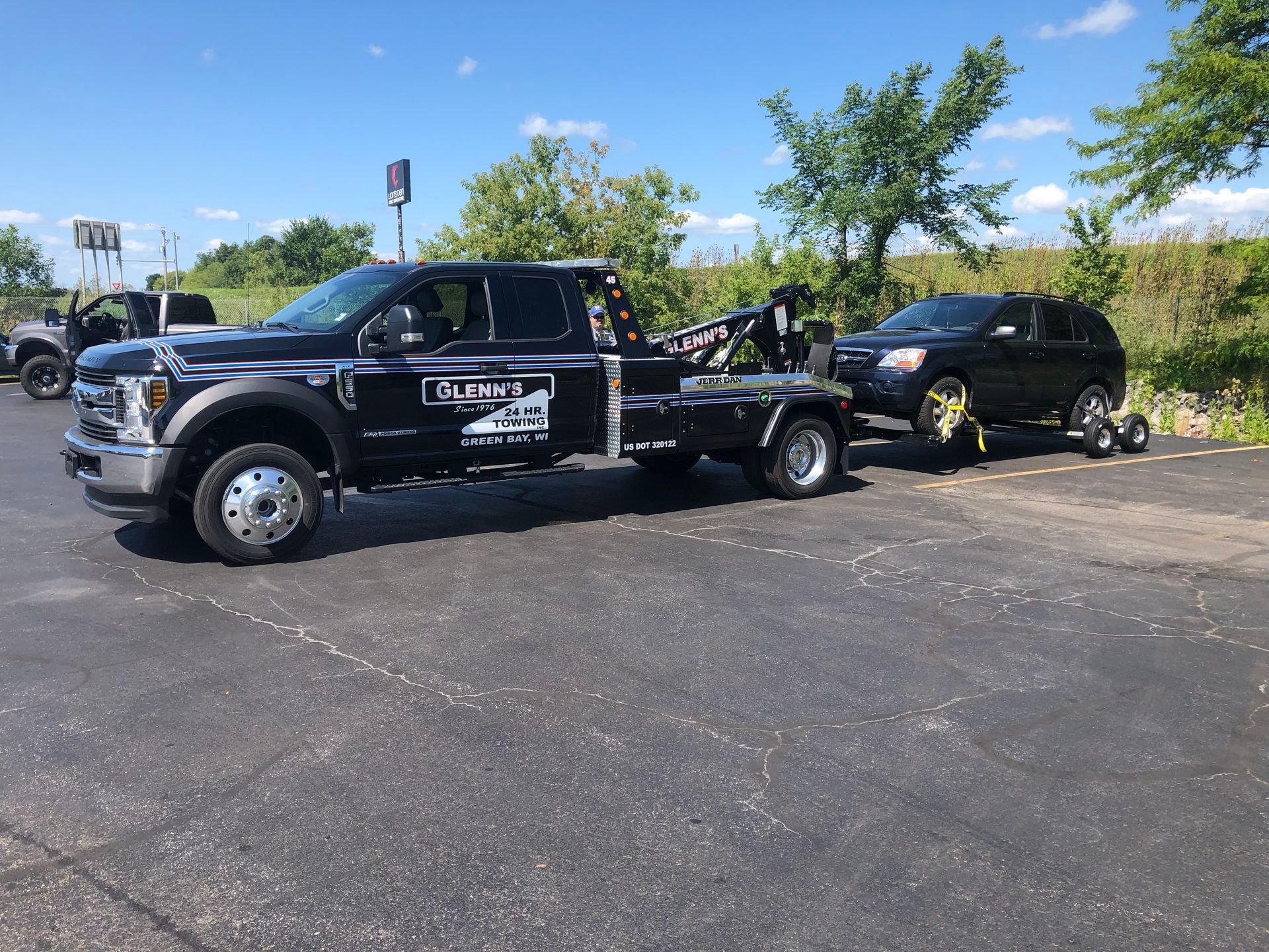 Black tow truck towing a black SUV on a sunny day.