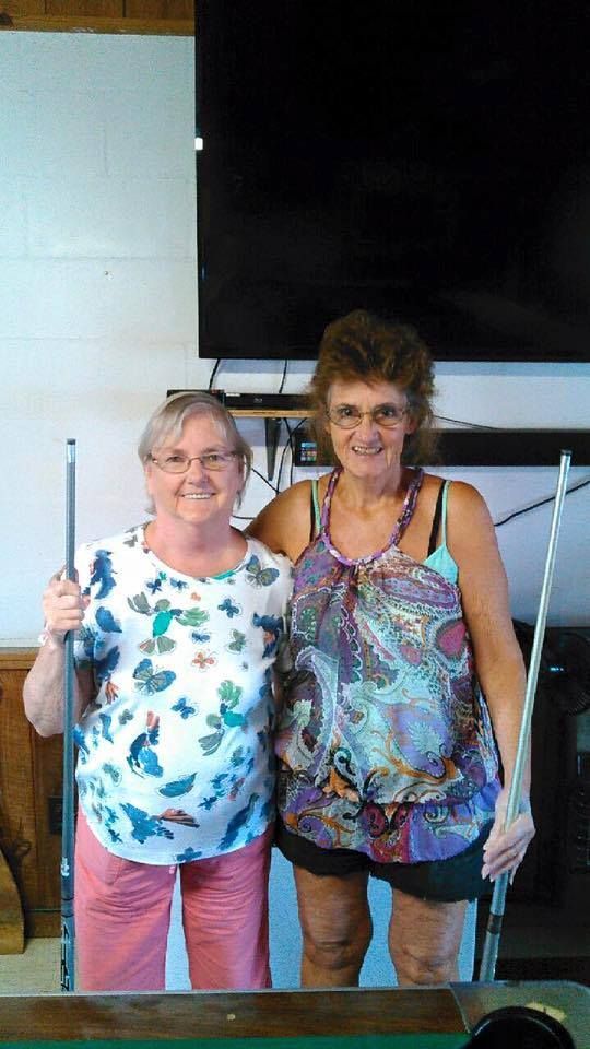 two women standing next to each other holding pool cues