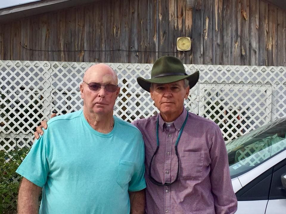 two men standing next to each other with one wearing a cowboy hat