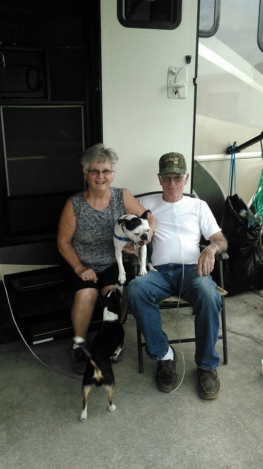 a man in a camo hat sits next to a woman holding a dog