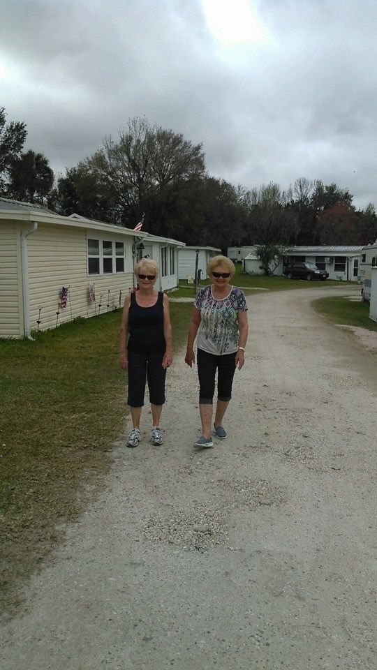 two women walking down a dirt road in front of mobile homes