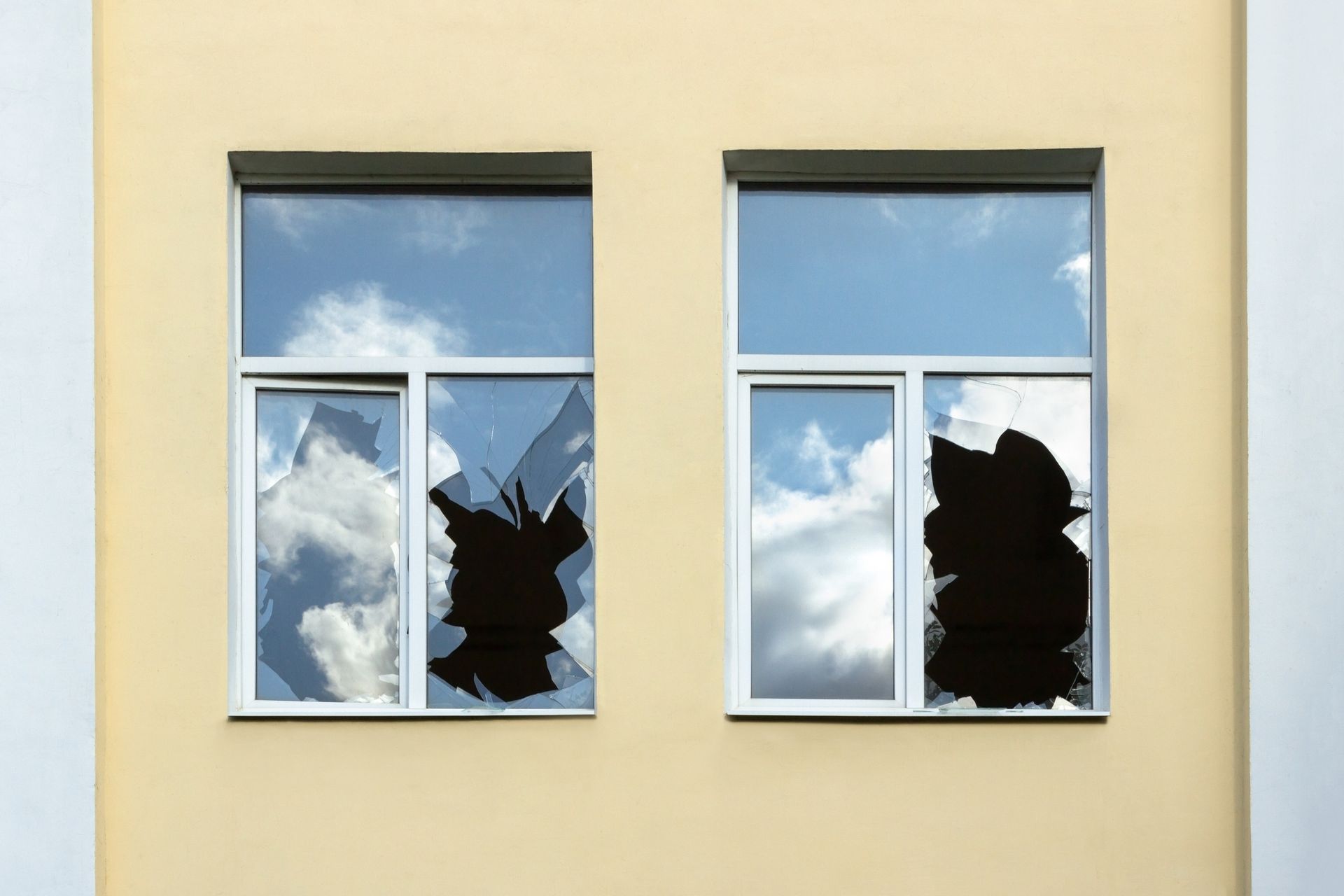 Two broken windowpanes reflect a moody, overcast sky. Two broken windowpanes reflect a moody, overcast sky.