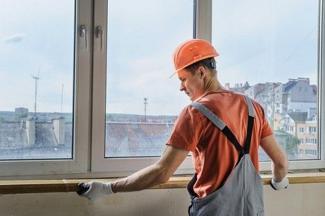 Male worker in safety gear installs a window sill inside a building.